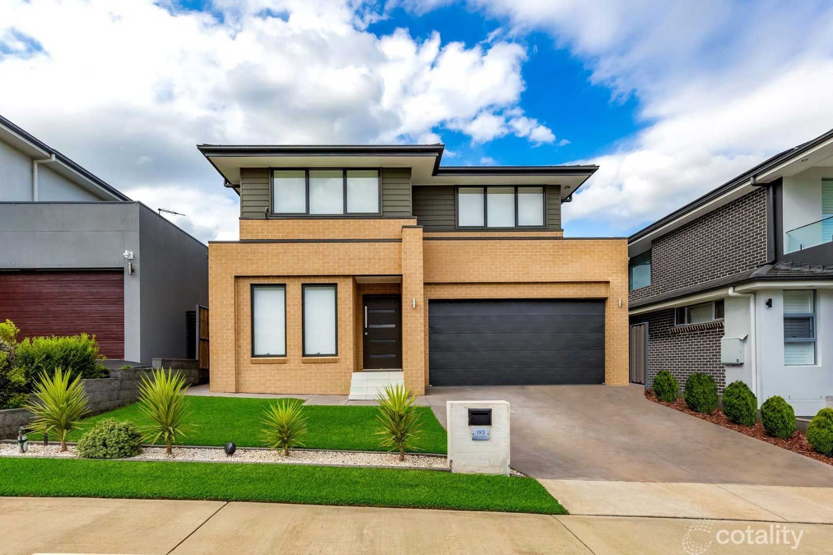 Two-story modern home with brick facade, black garage door, and green lawn under a partly cloudy sky.