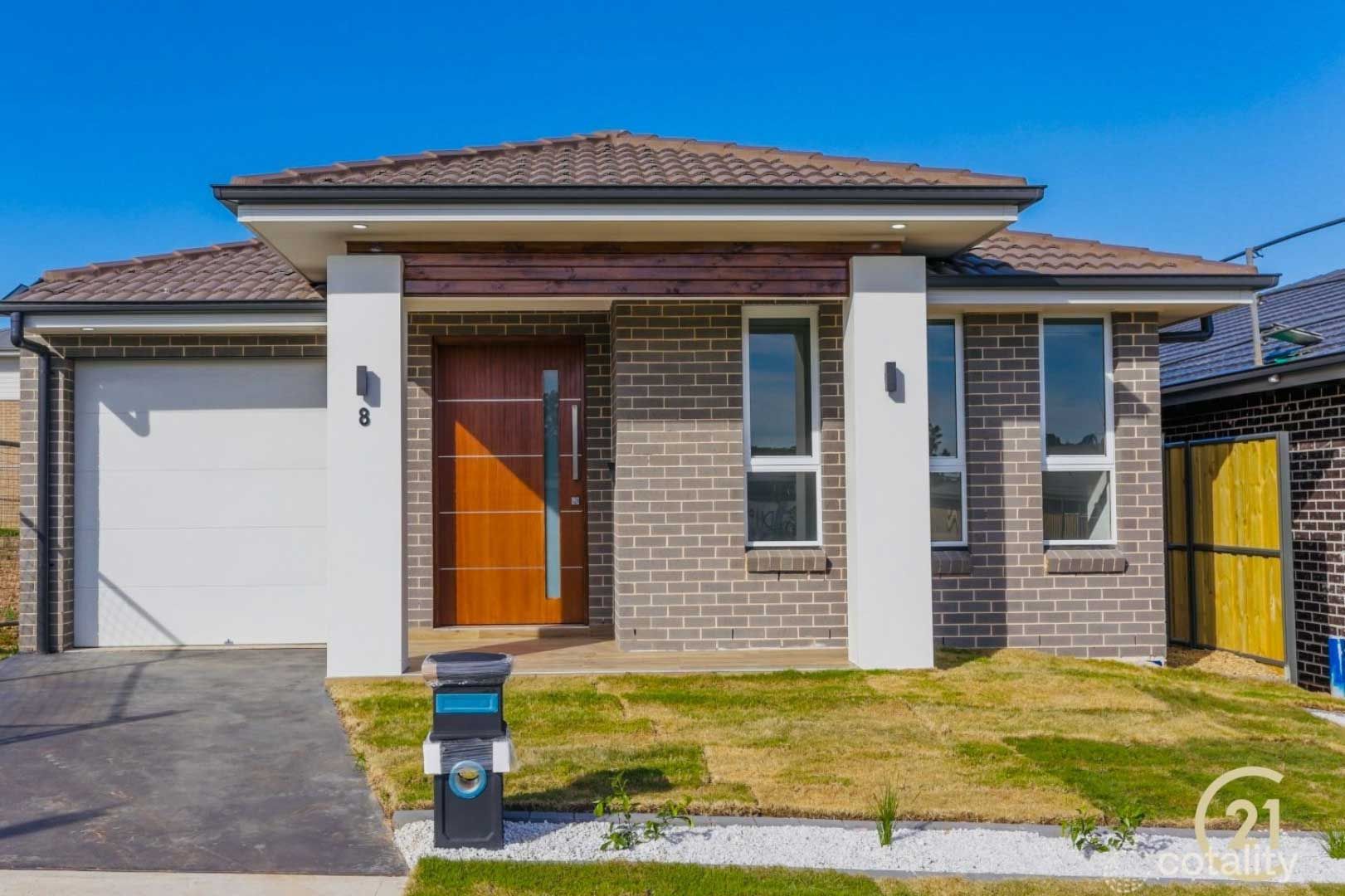 Modern single-story brick house with brown roof and wooden door, white pillars, and mailbox on a sunny day.
