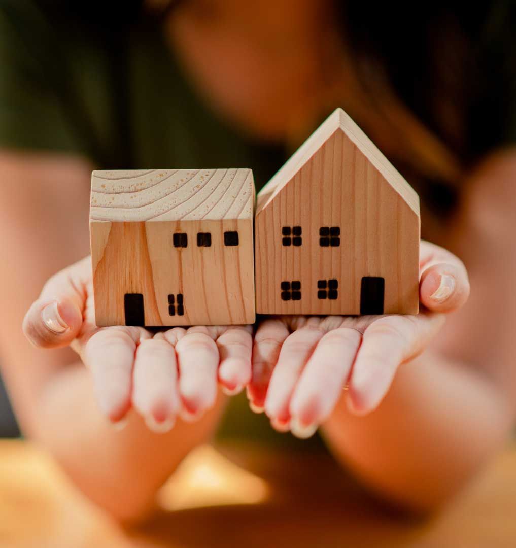 Person holding two wooden house miniatures.