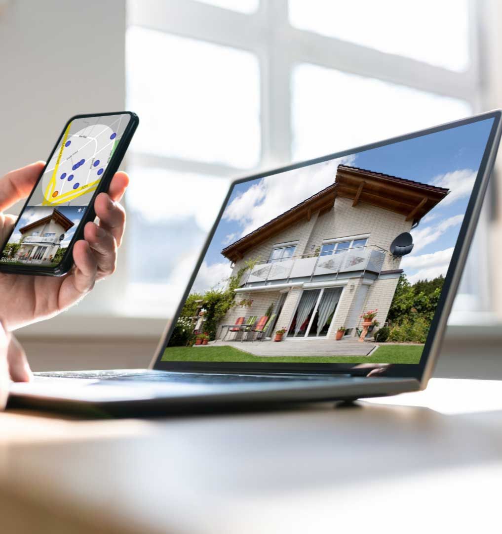 Person holding phone displaying house, laptop shows same house.
