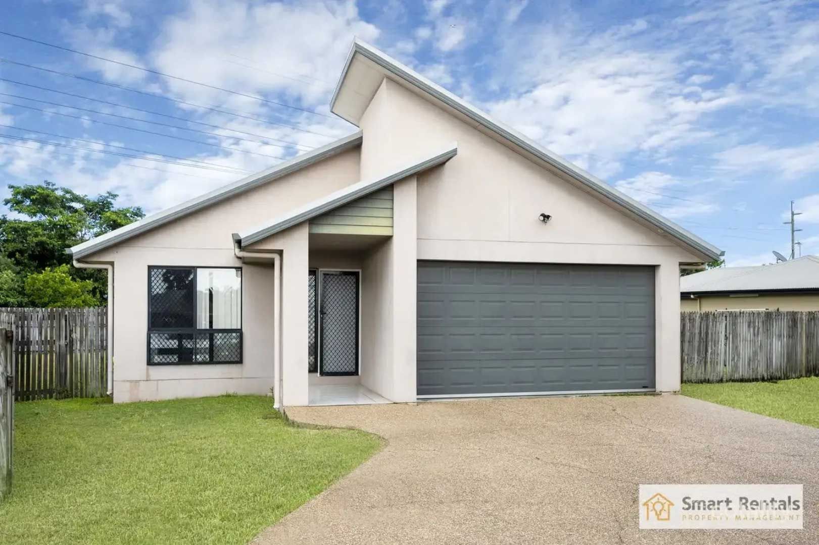 Beige house with a grey garage door and a gravel driveway, under a cloudy sky.