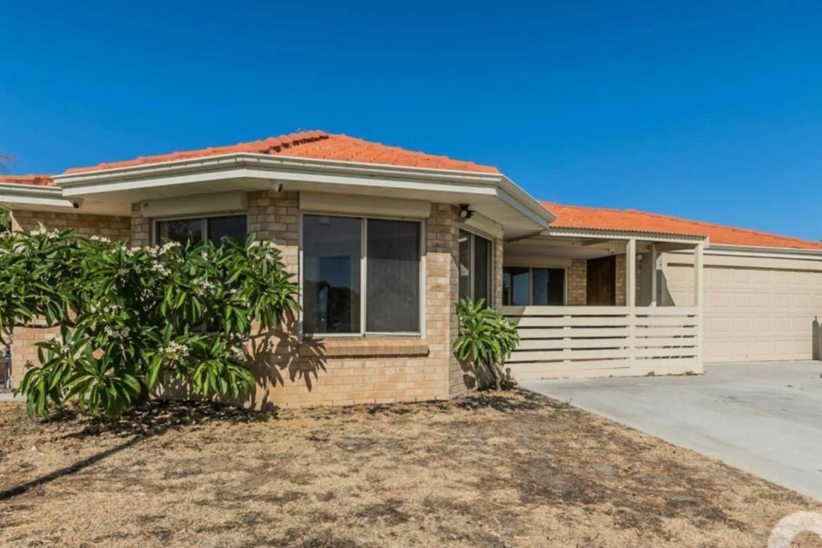 Suburban home with orange tile roof, beige brick facade, blue sky, and driveway.