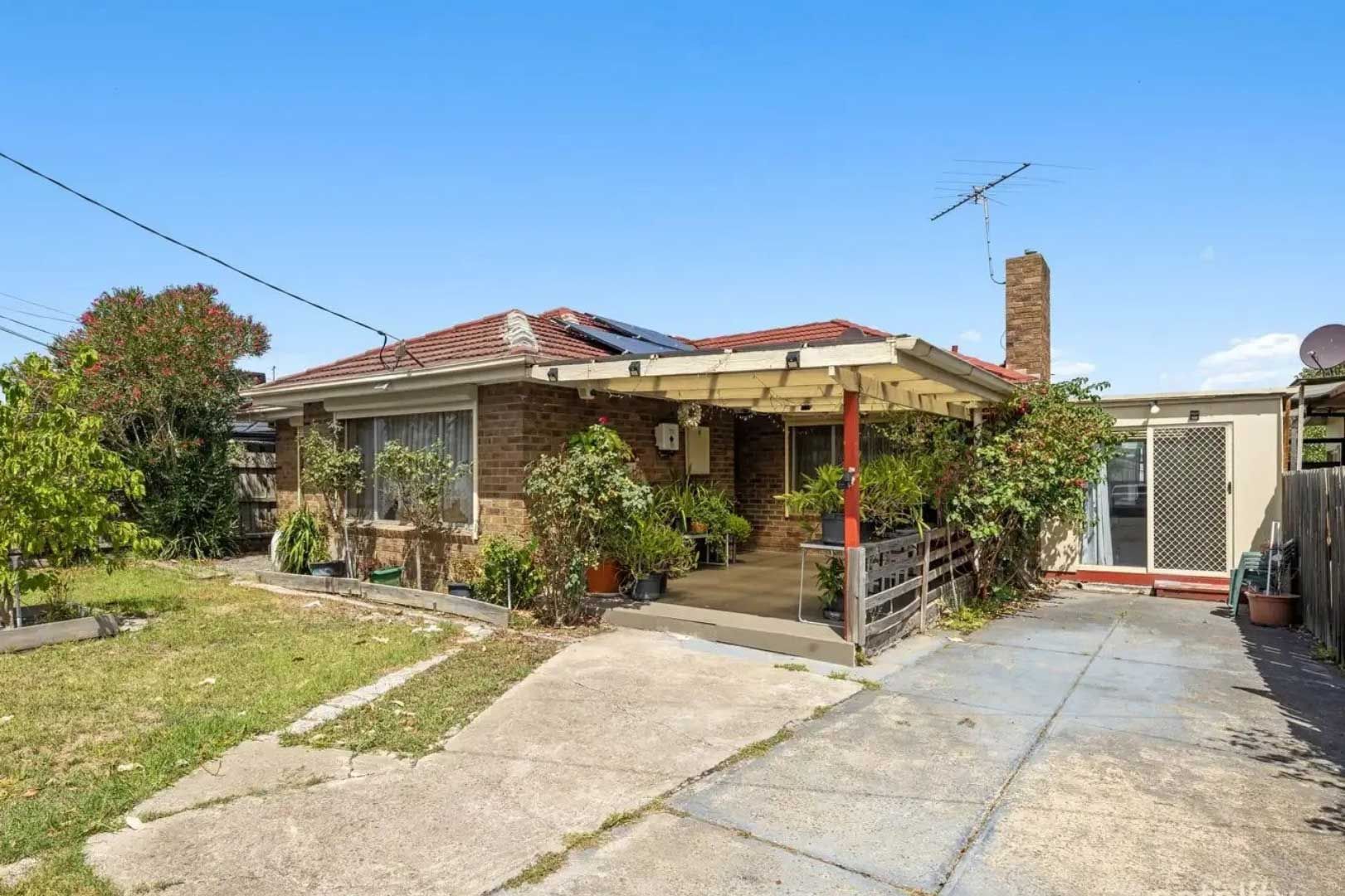 Brick house with concrete driveway and porch, plants in front. Sunny day.