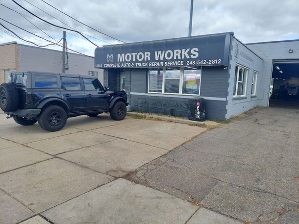 A black jeep is parked in front of a motor works auto and truck repair shop. | Motor Works