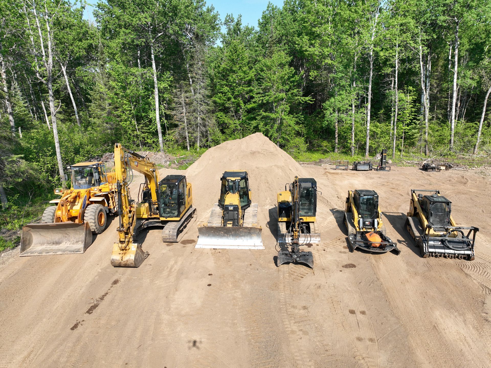 A group of construction vehicles are lined up on a dirt road.