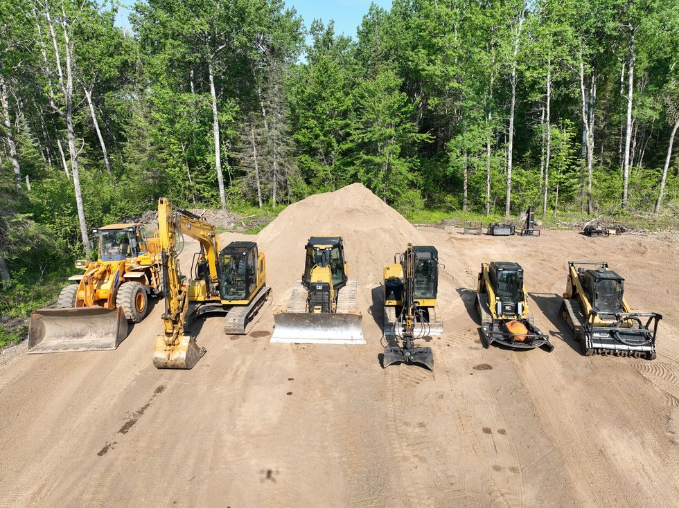 A group of construction vehicles are lined up on a dirt road.