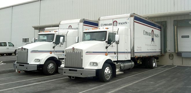 Two kenworth trucks are parked next to each other in a parking lot from Cupboard Wagon cabinet delivery services