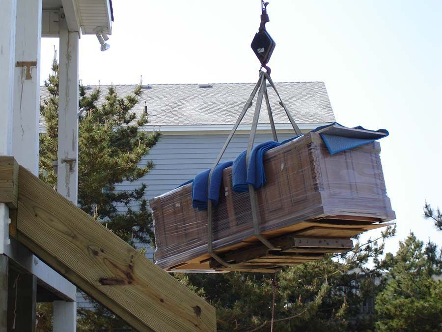 A large wooden box is being lifted by a crane from Cupboard Wagon cabinet delivery services