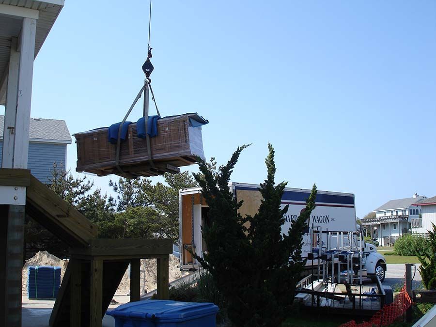A large box is being lifted by a crane in front of a moving truck from Cupboard Wagon cabinet delivery services