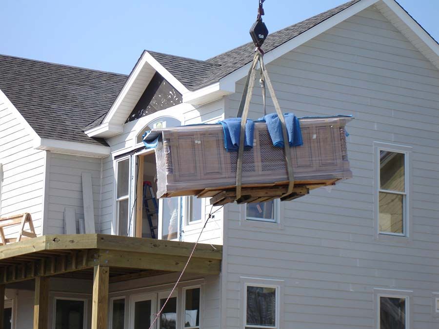 A crane is lifting a bathtub into a house from Cupboard Wagon cabinet delivery services
