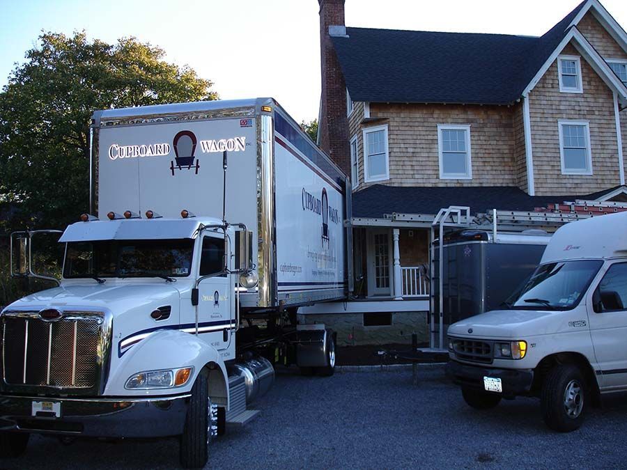 A white truck is parked in front of a large house from Cupboard Wagon cabinet delivery services