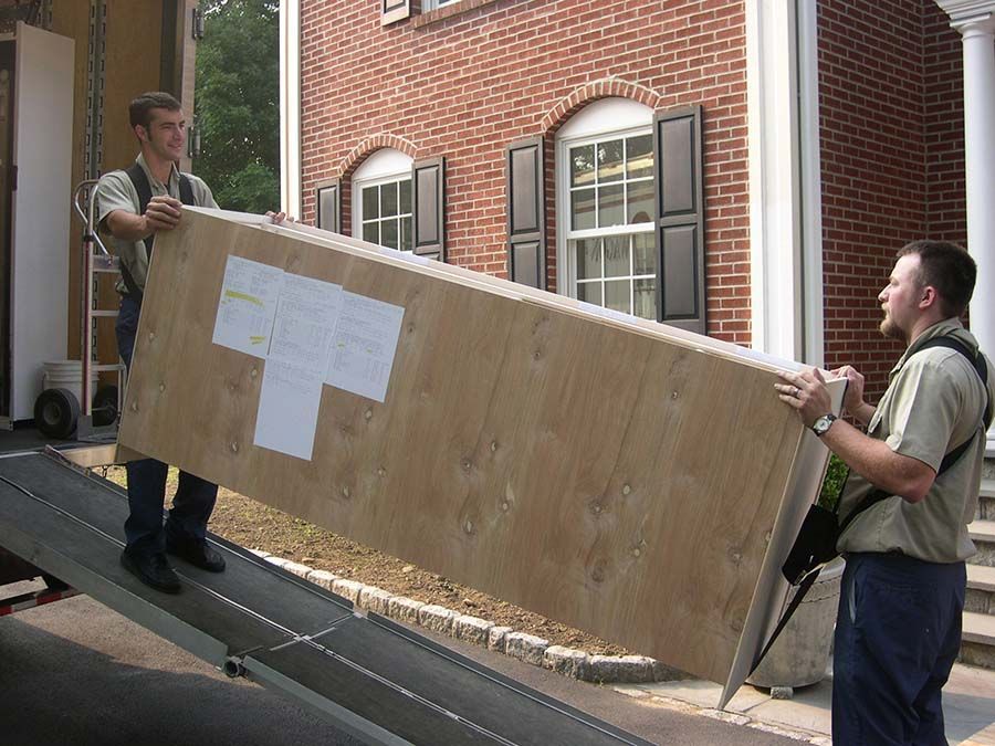 Two men are carrying a large piece of wood on a ramp from Cupboard Wagon cabinet delivery services