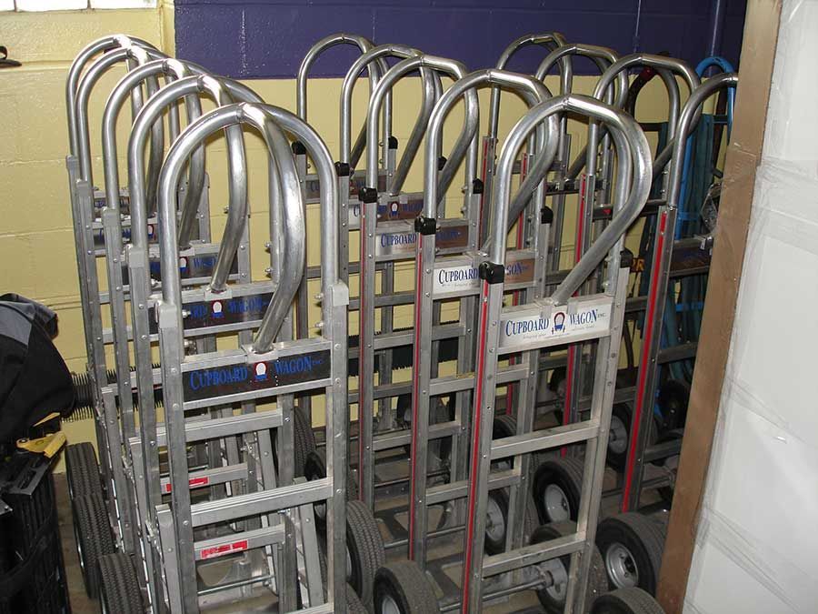 A bunch of hand trucks are lined up in a room from Cupboard Wagon cabinet delivery services