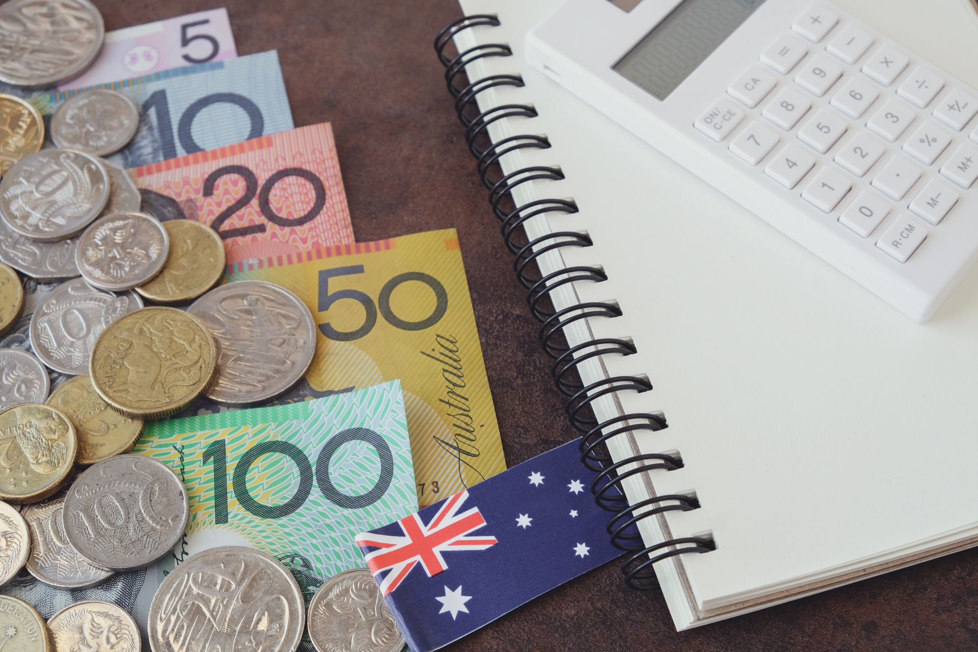 Australian currency, coins and notes, with a calculator, notepad, and flag.