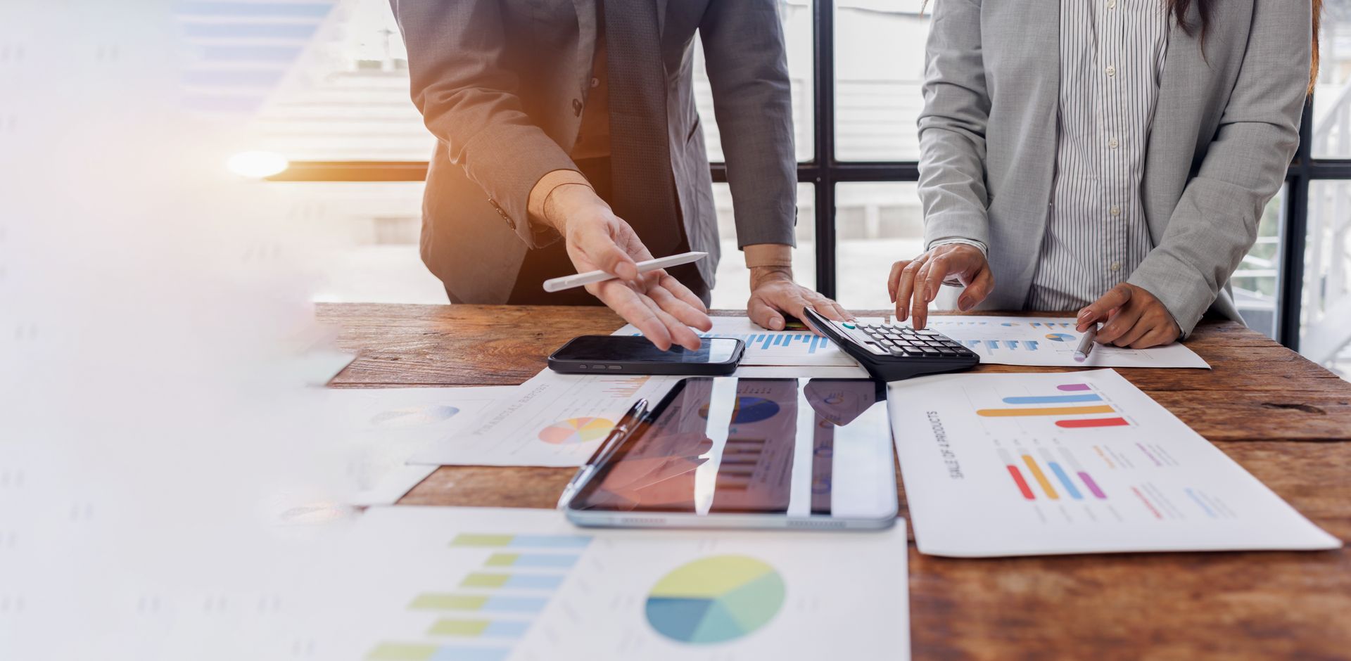 People in business attire working on financial documents and a calculator at a wooden table.