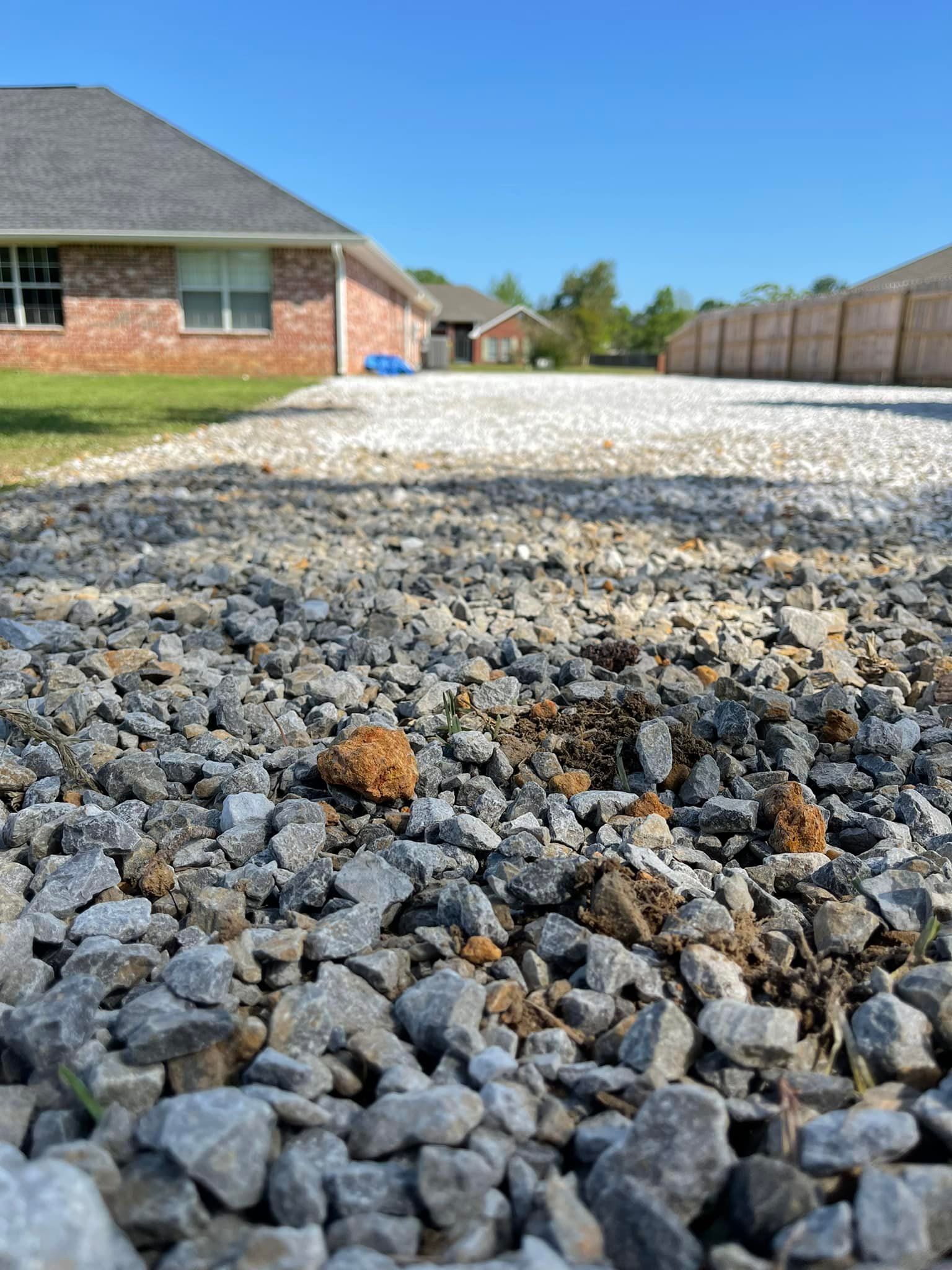 Close-up of gravel driveway leading towards houses under a blue sky.