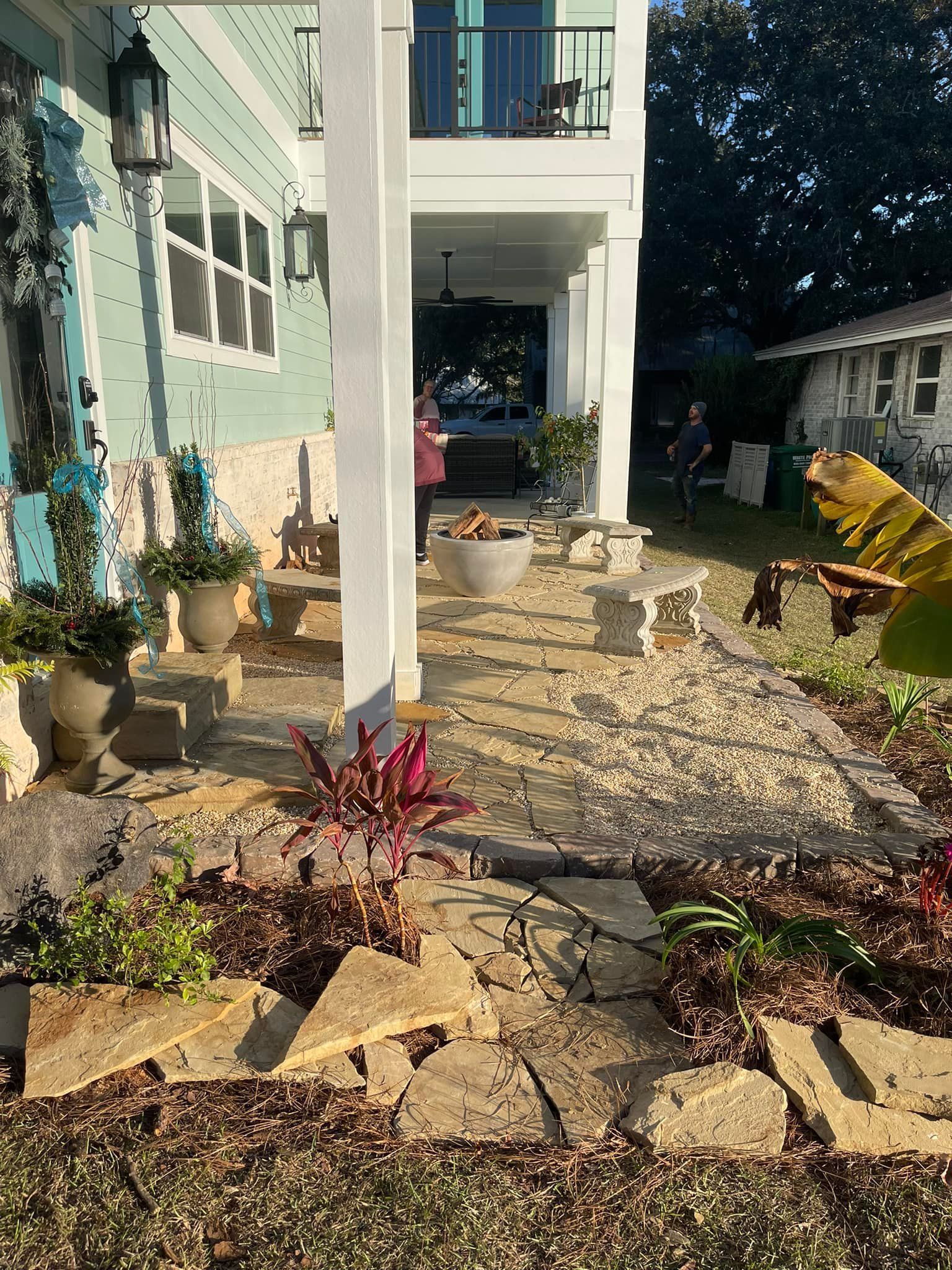 Pathway with stone pavers leading to porch with two people and potted plants.