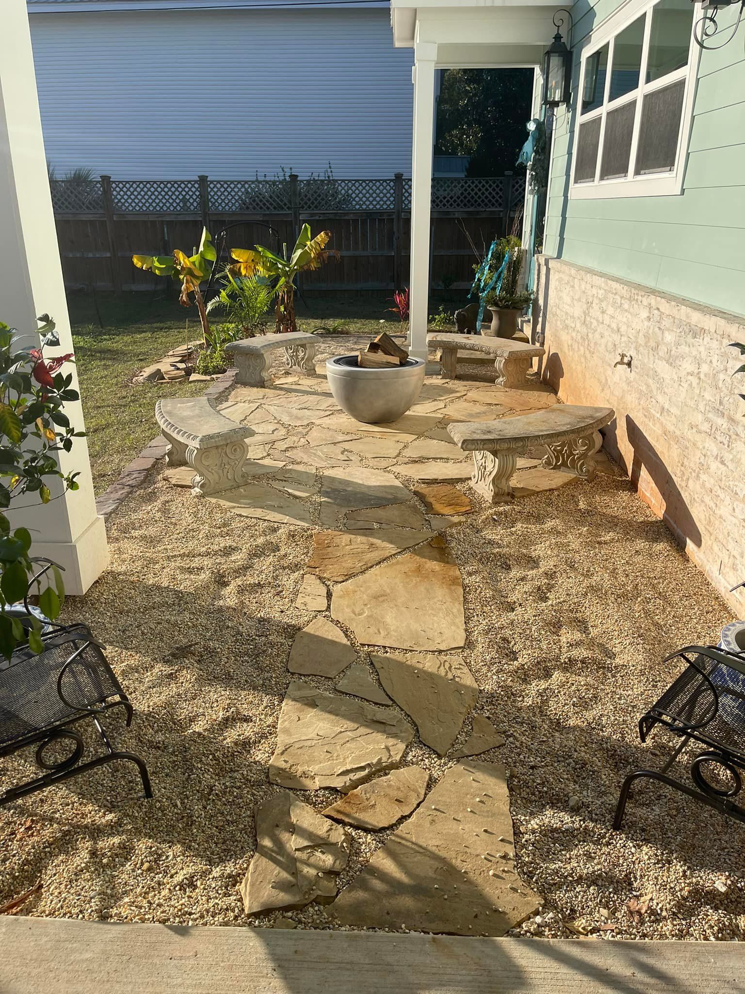 Stone patio and path with gravel, small plants, and a light-colored porch.