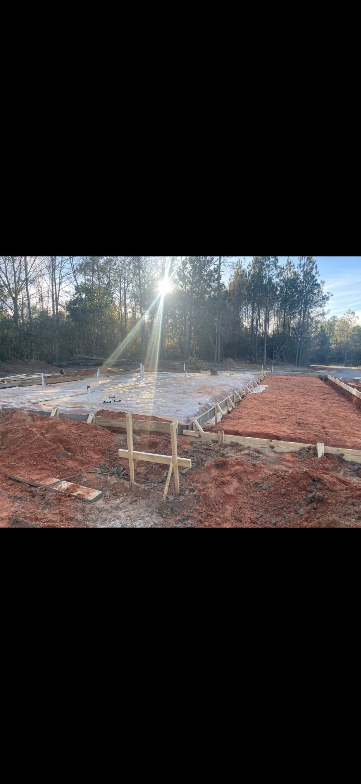 Construction site with exposed dirt, wooden supports, and sunlight in the background.