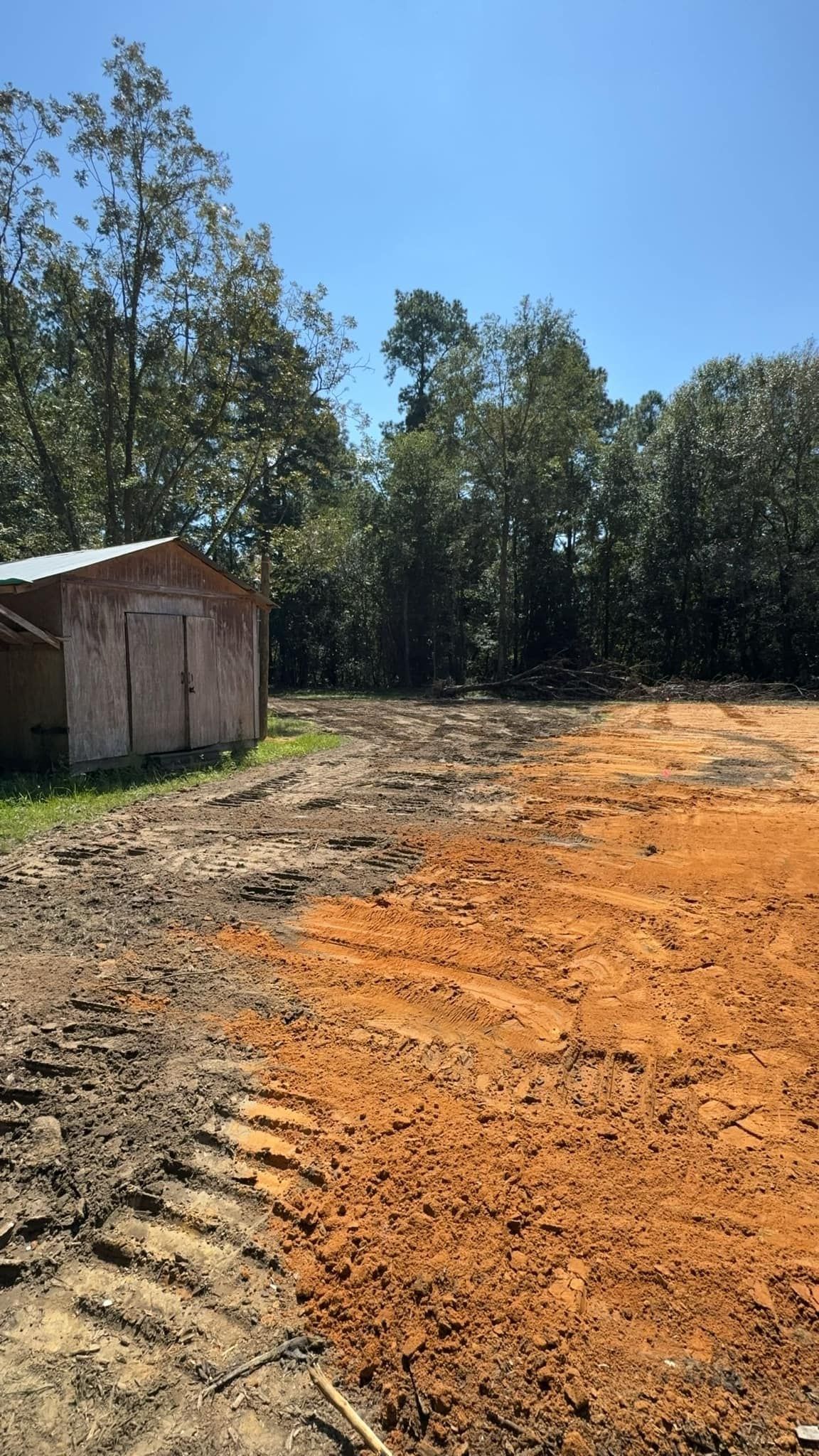 Dirt clearing next to a small brick building, surrounded by trees under a blue sky.