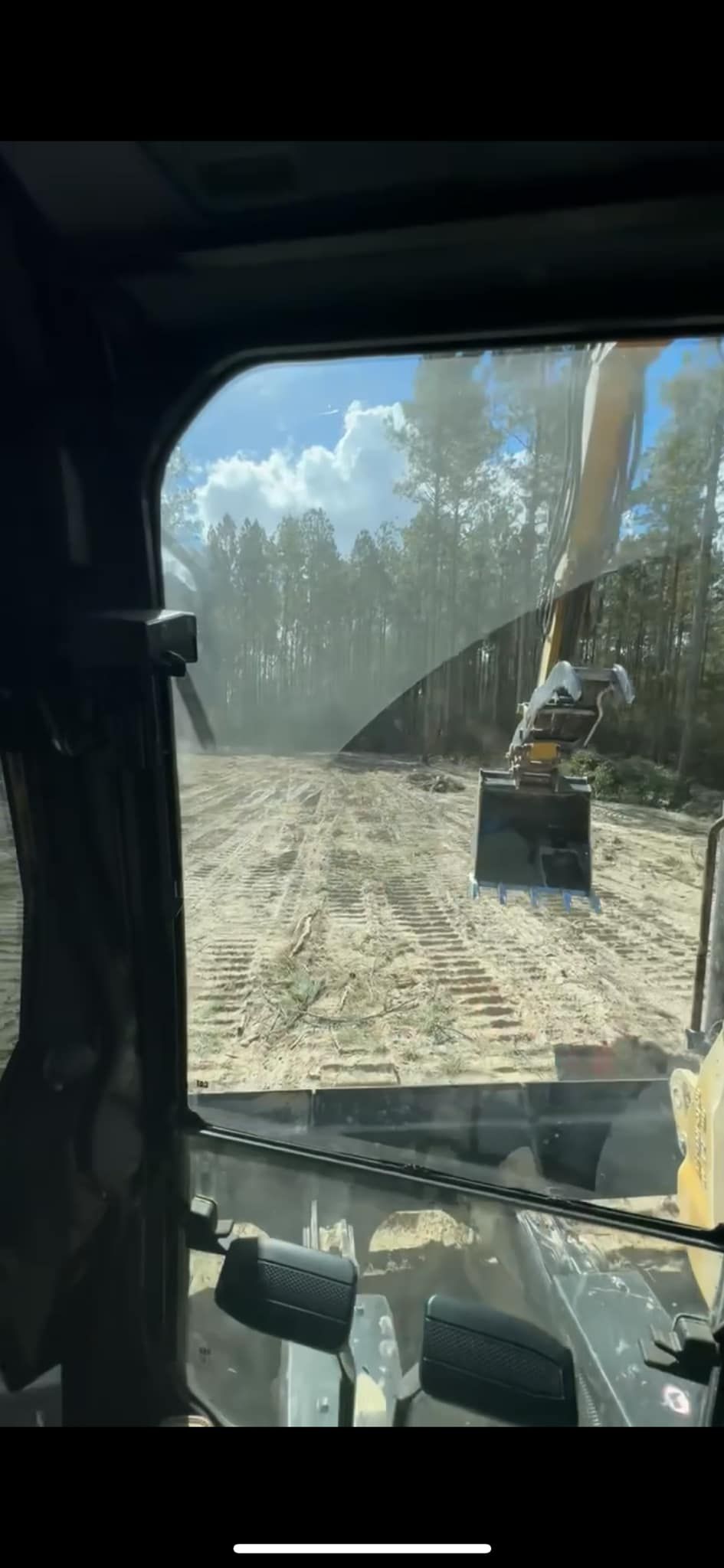 View from inside heavy machinery. Trees being cleared, dust in the air.