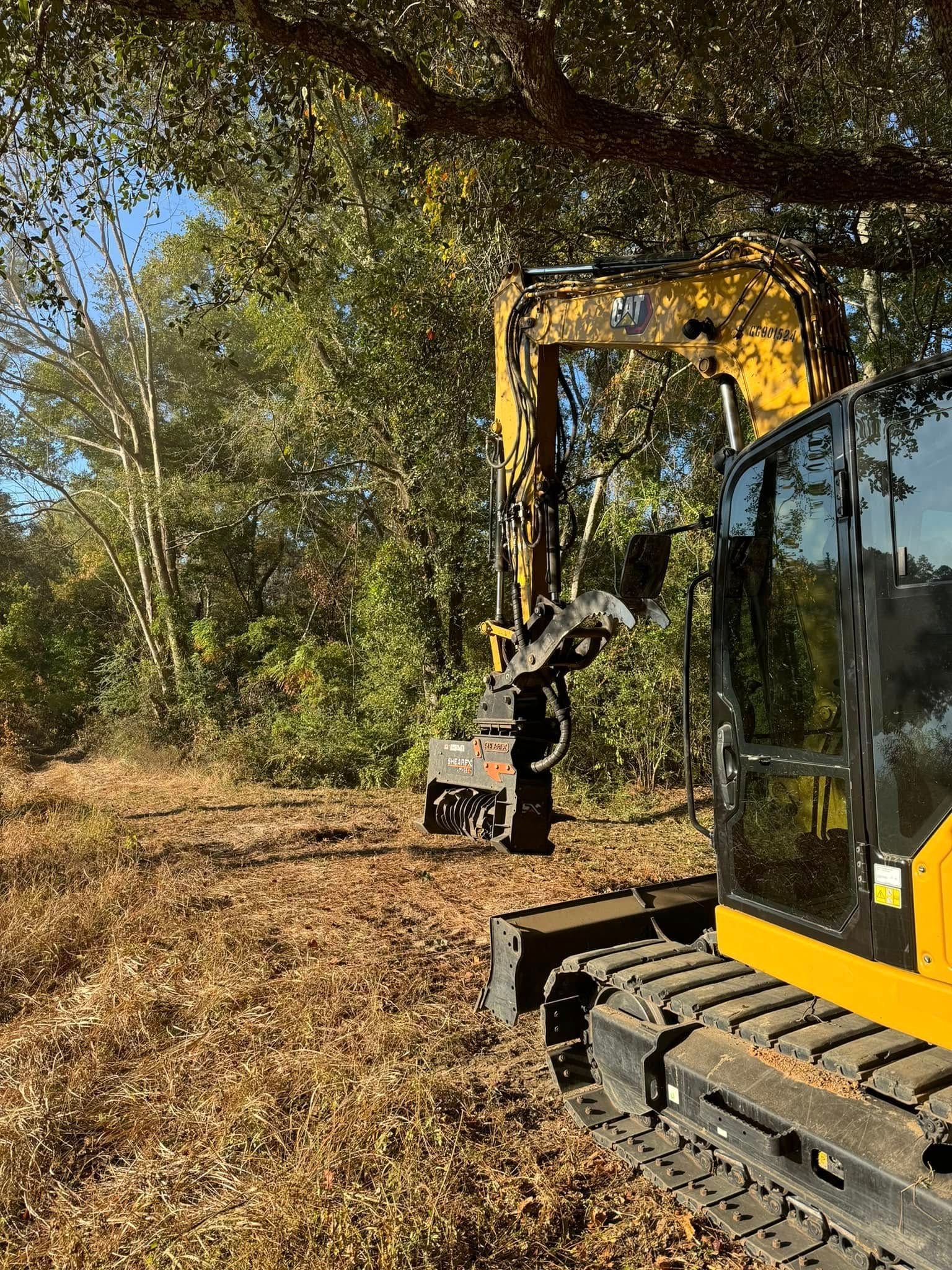 Yellow excavator clearing brush in a wooded area. Sunny day.