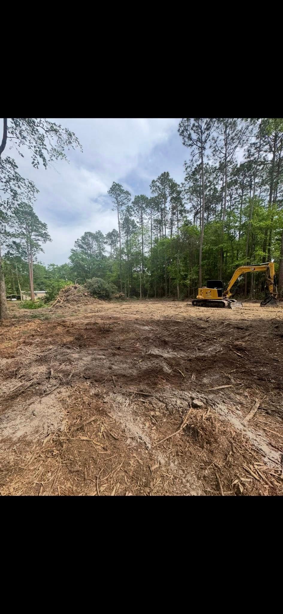 An area cleared of trees for construction, with a yellow excavator in the background and a cloudy sky.