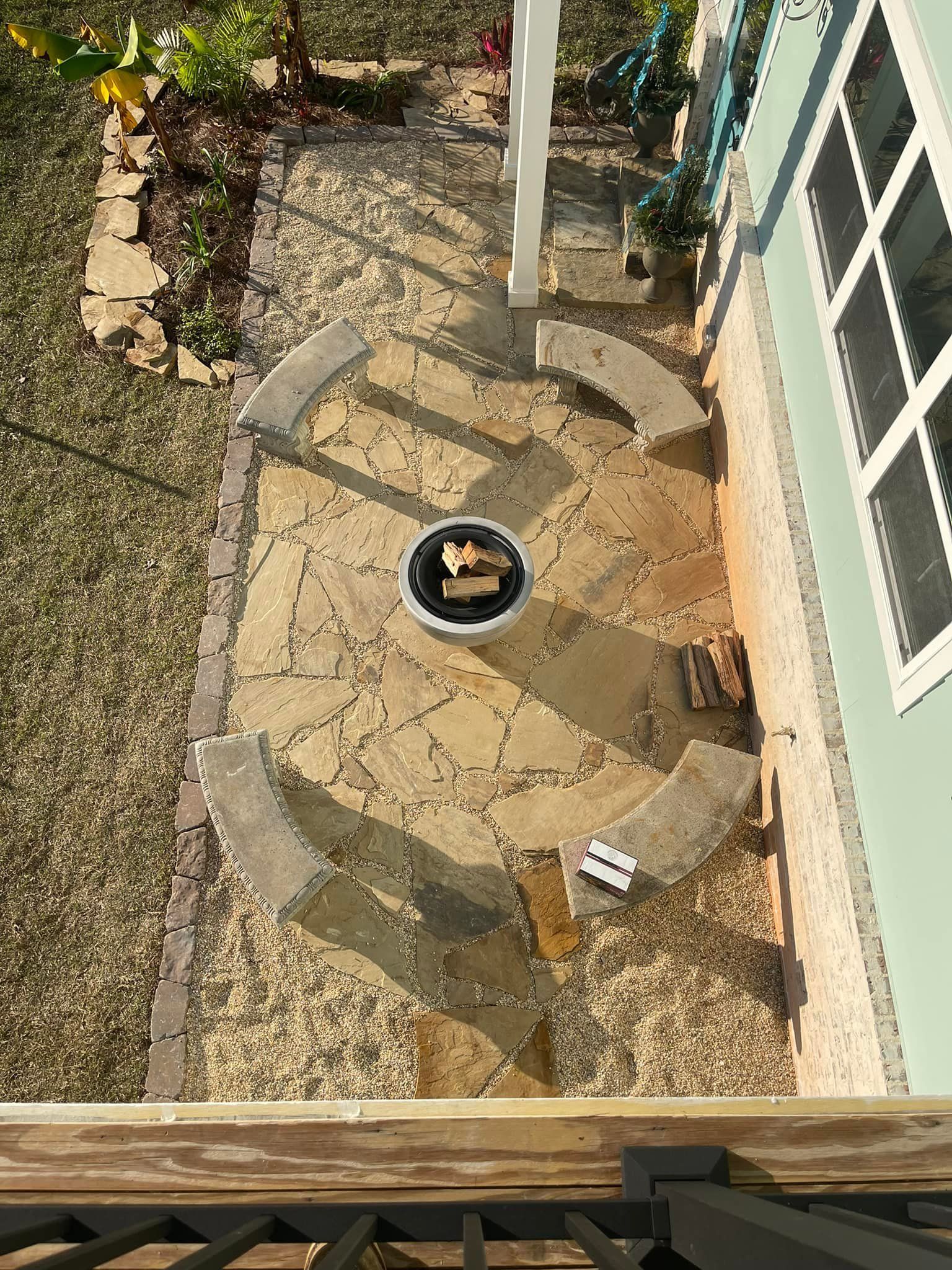 Overhead view of a circular stone patio with a fire pit, surrounded by curved benches and landscaping.
