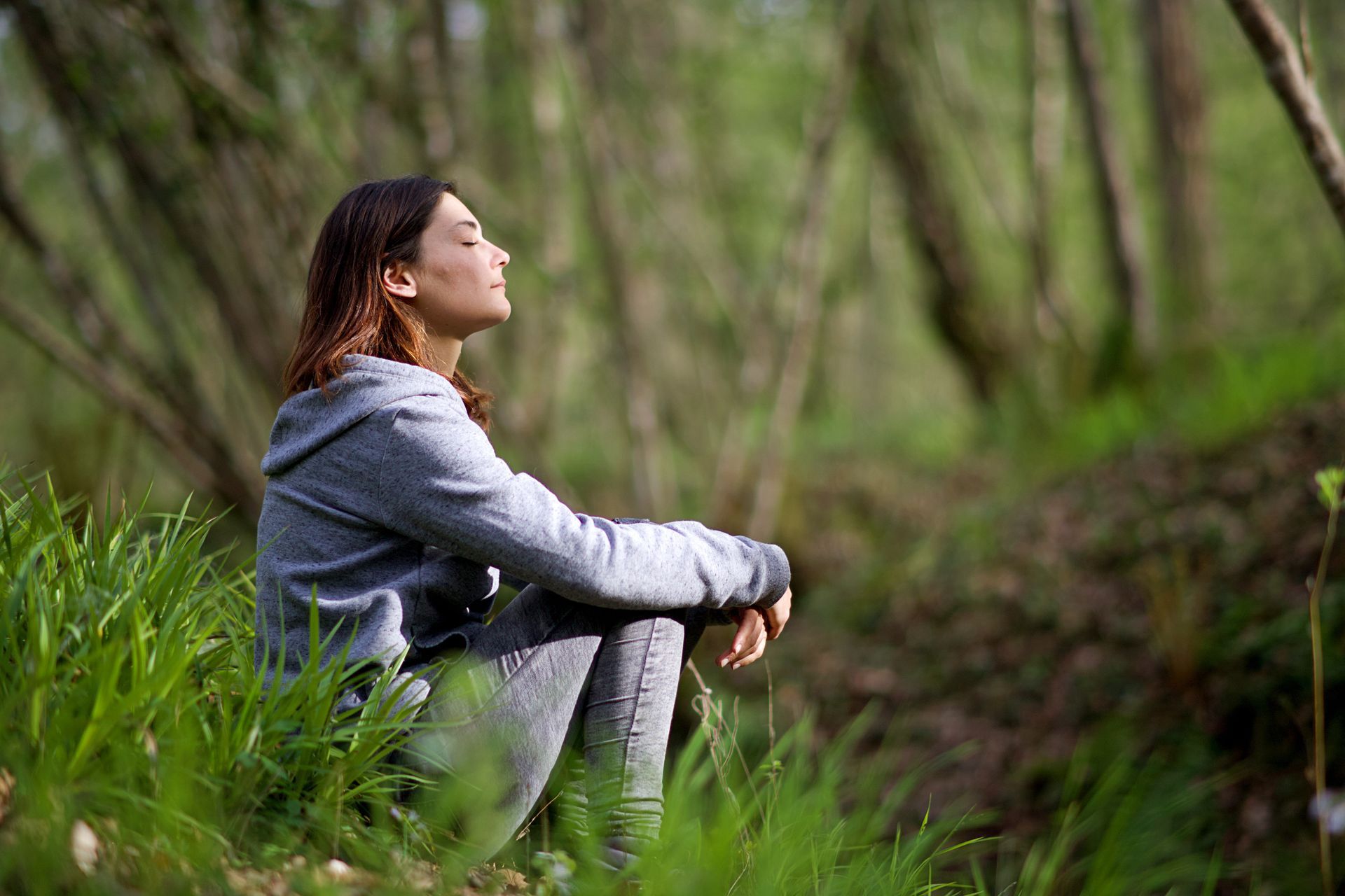 Person sitting in a forest, gazing upward in a gray jacket and leggings.