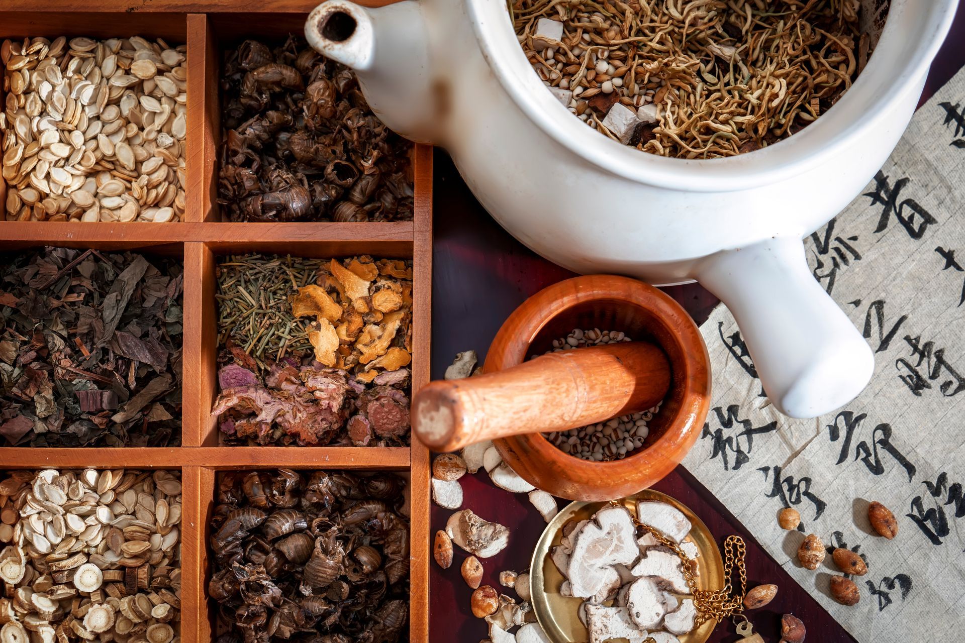 Herbal tea ingredients in wooden trays with mortar and pestle on a patterned cloth.