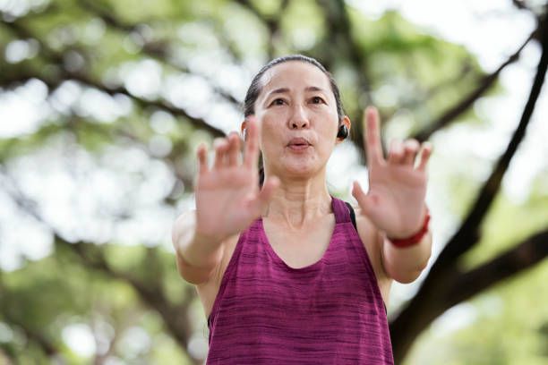 Woman in purple tank top outdoors, arms outstretched, palms forward.