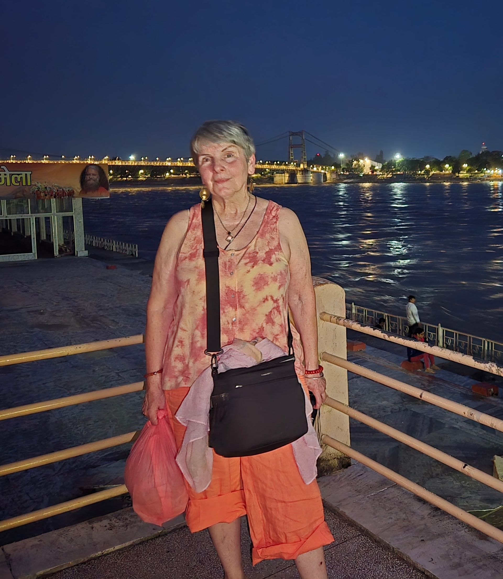 Woman in patterned shawl stands in front of woven archway, smiles.
