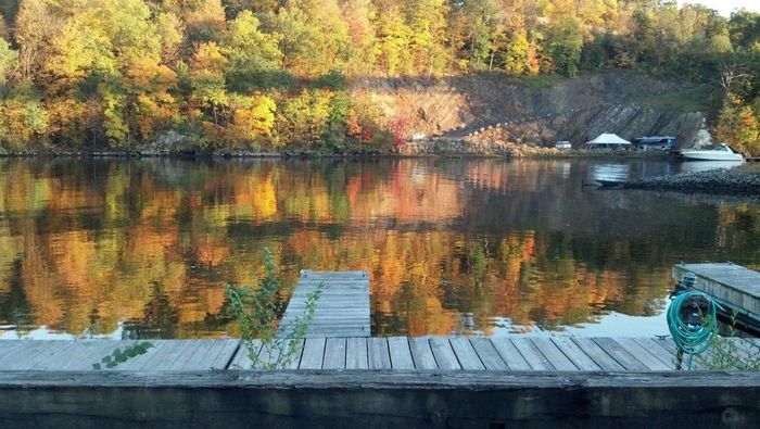 Autumn trees reflected in calm lake water under a blue sky.