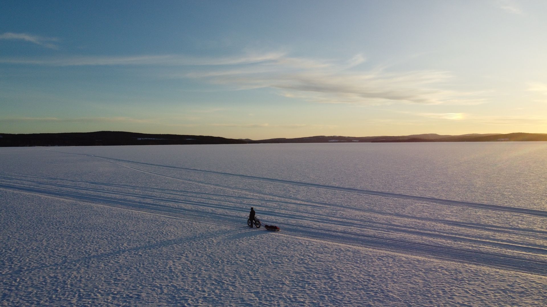 An aerial view of a person walking a dog in a snowy field.