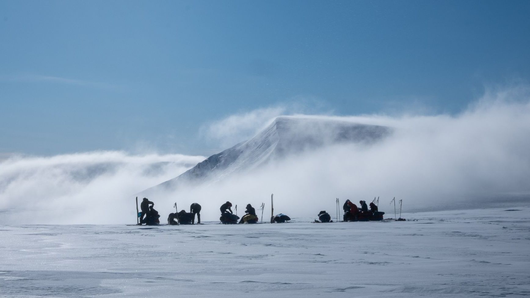 A group of people are standing in the snow in front of a mountain.