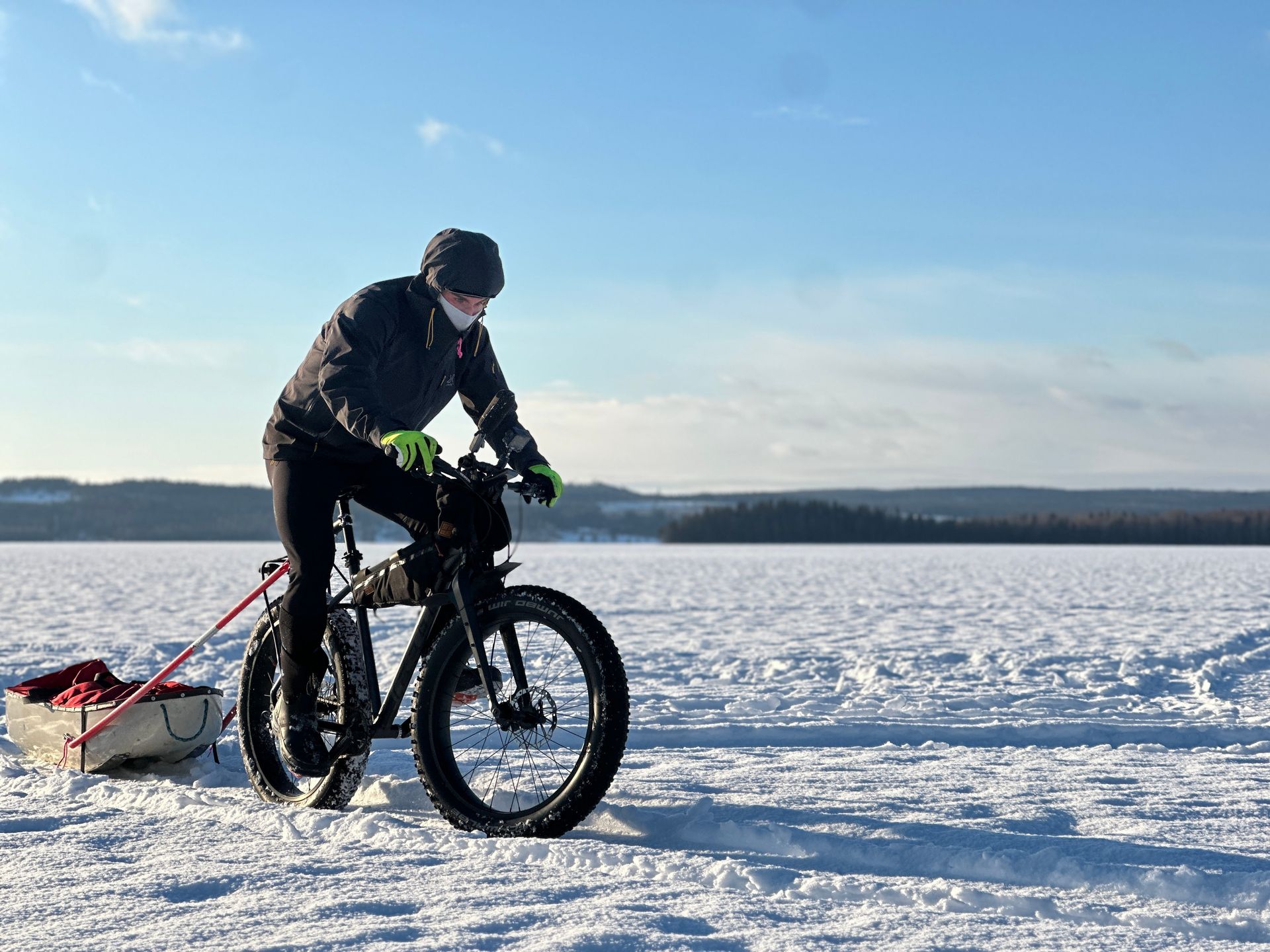 A man is riding a bike in the snow with a sled pulling it.