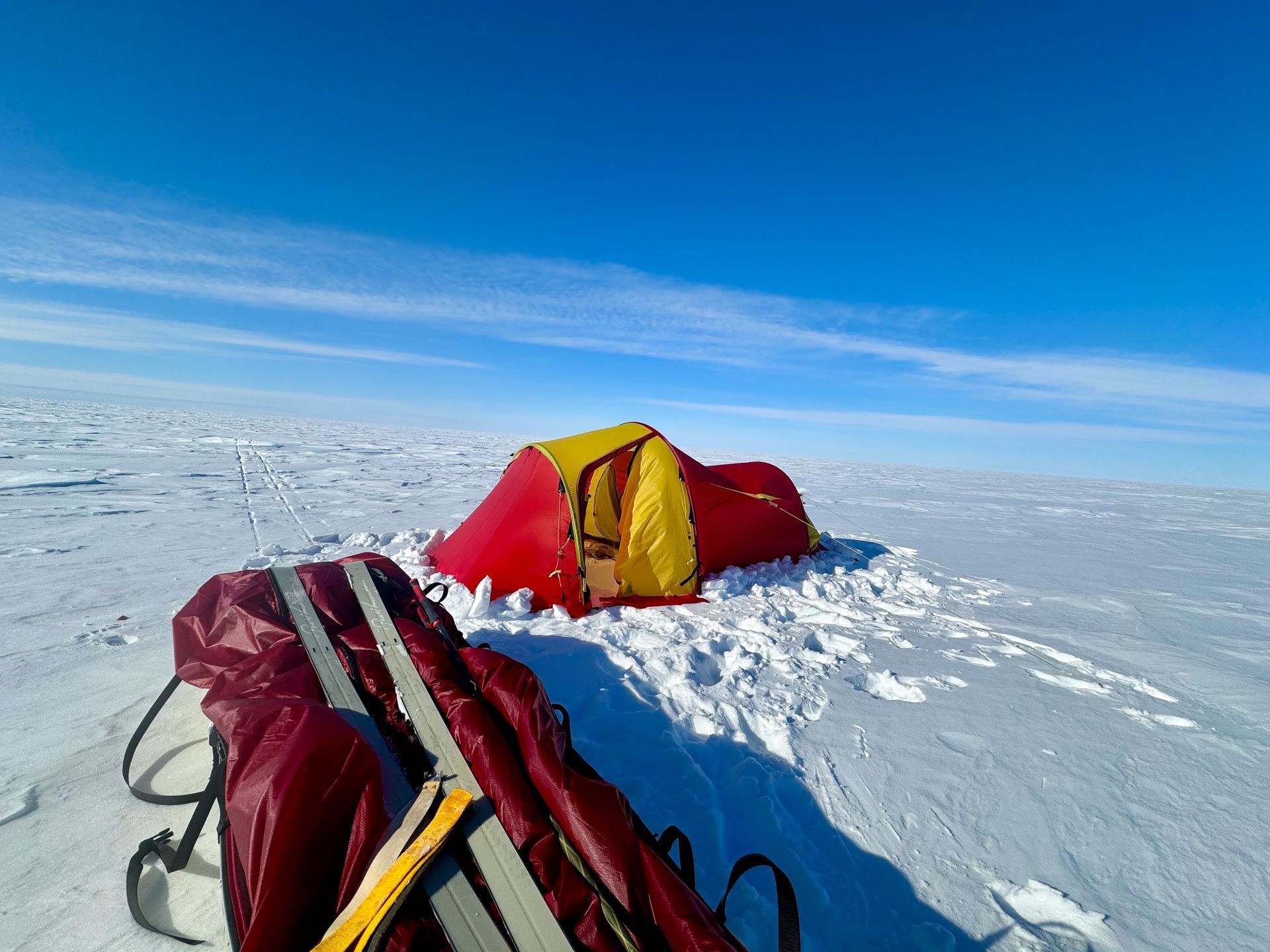 A red and yellow tent is sitting in the middle of a snowy field.