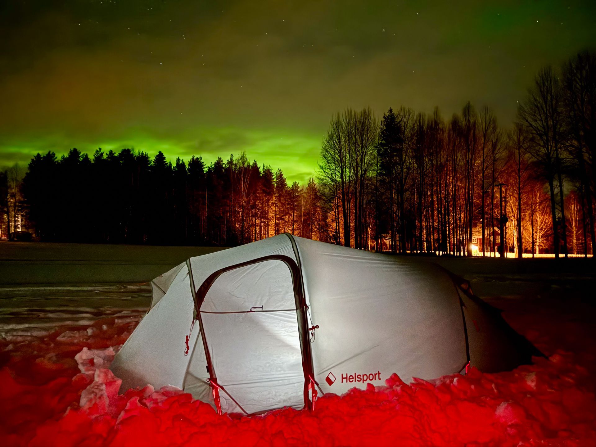 A tent is sitting in the snow with the aurora borealis in the background.