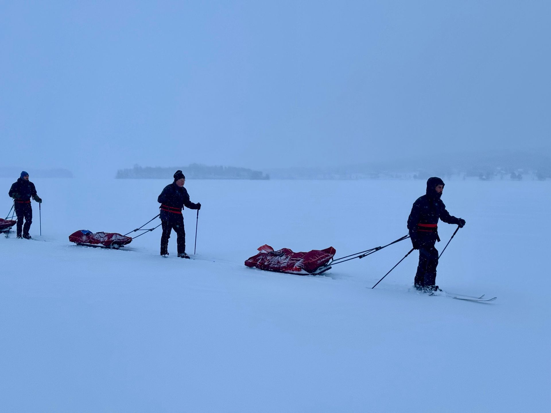 Three people skiing in the snow pulling a sled