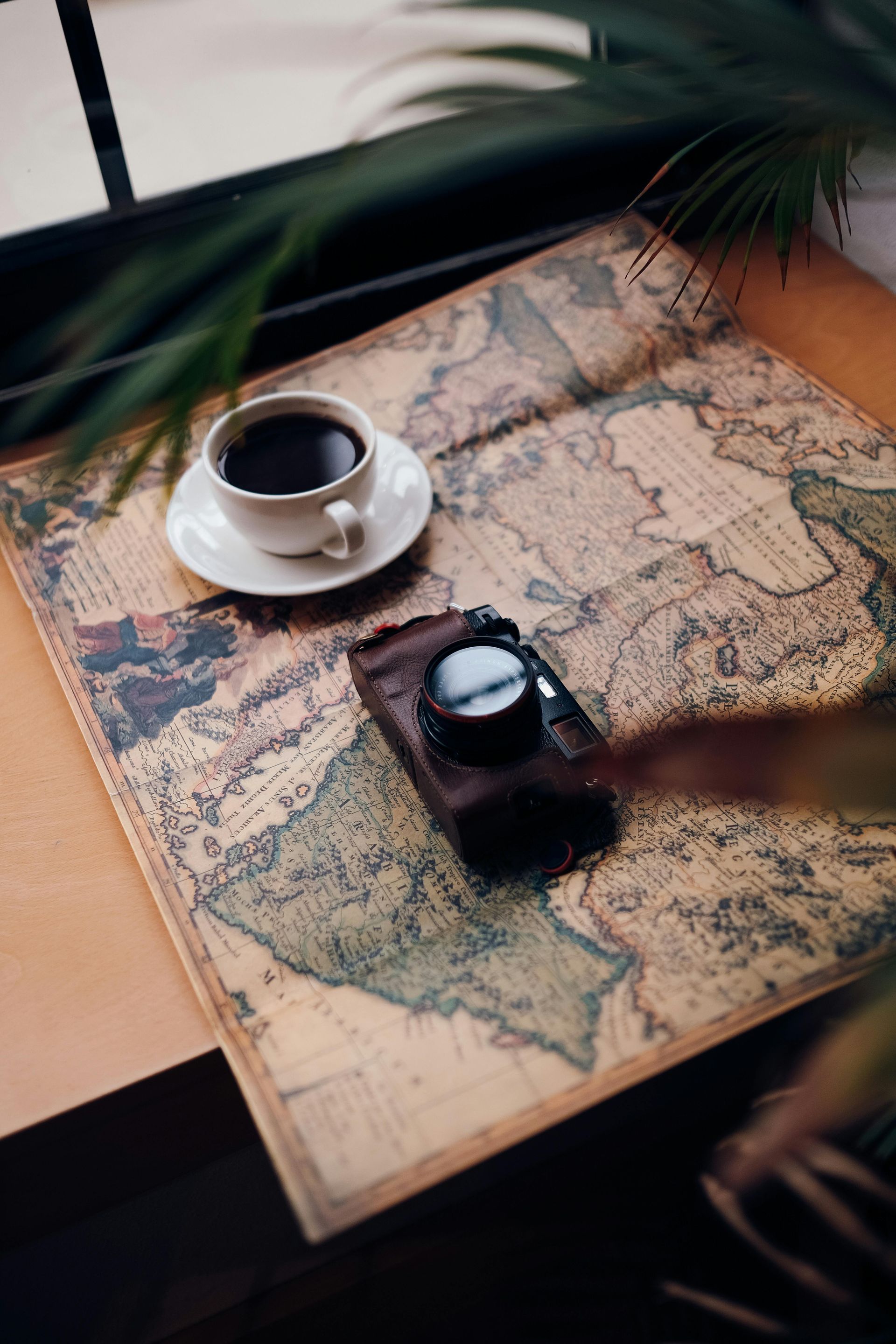A cup of coffee , a camera , and a map are on a table.