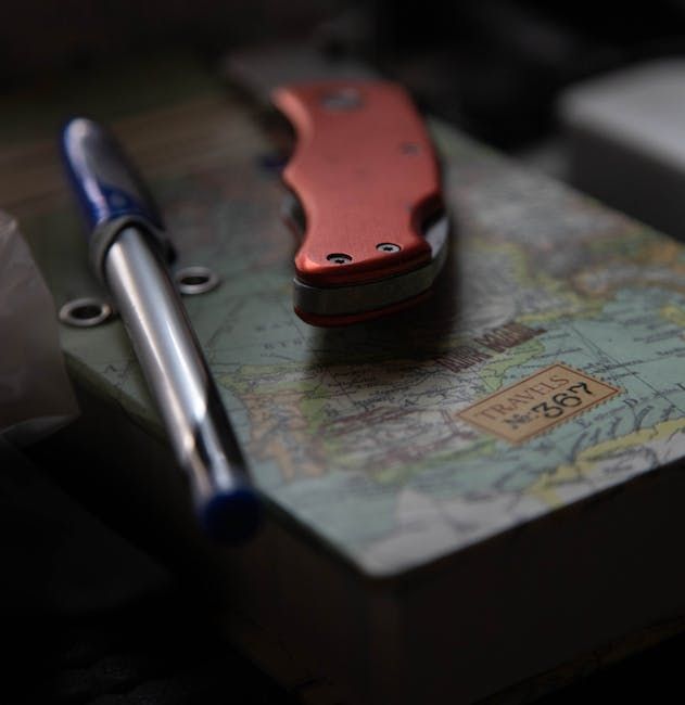 Pen and orange folding knife rest on a journal with a world map cover.