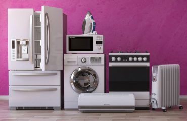 A refrigerator , washer , dryer , microwave , stove , and heater are sitting in a room.