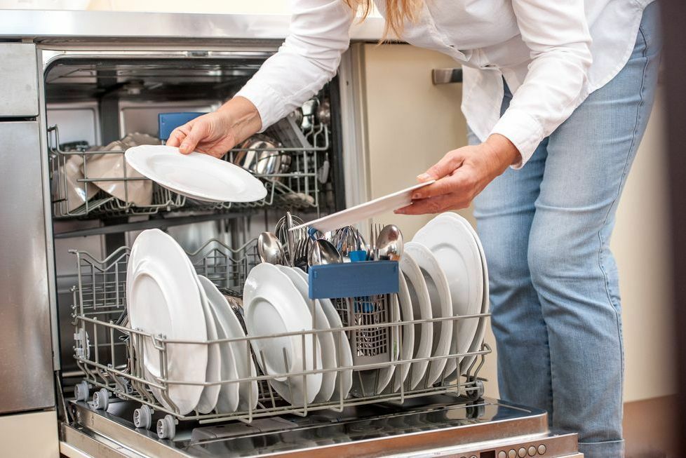 A woman is putting a plate in a dishwasher.