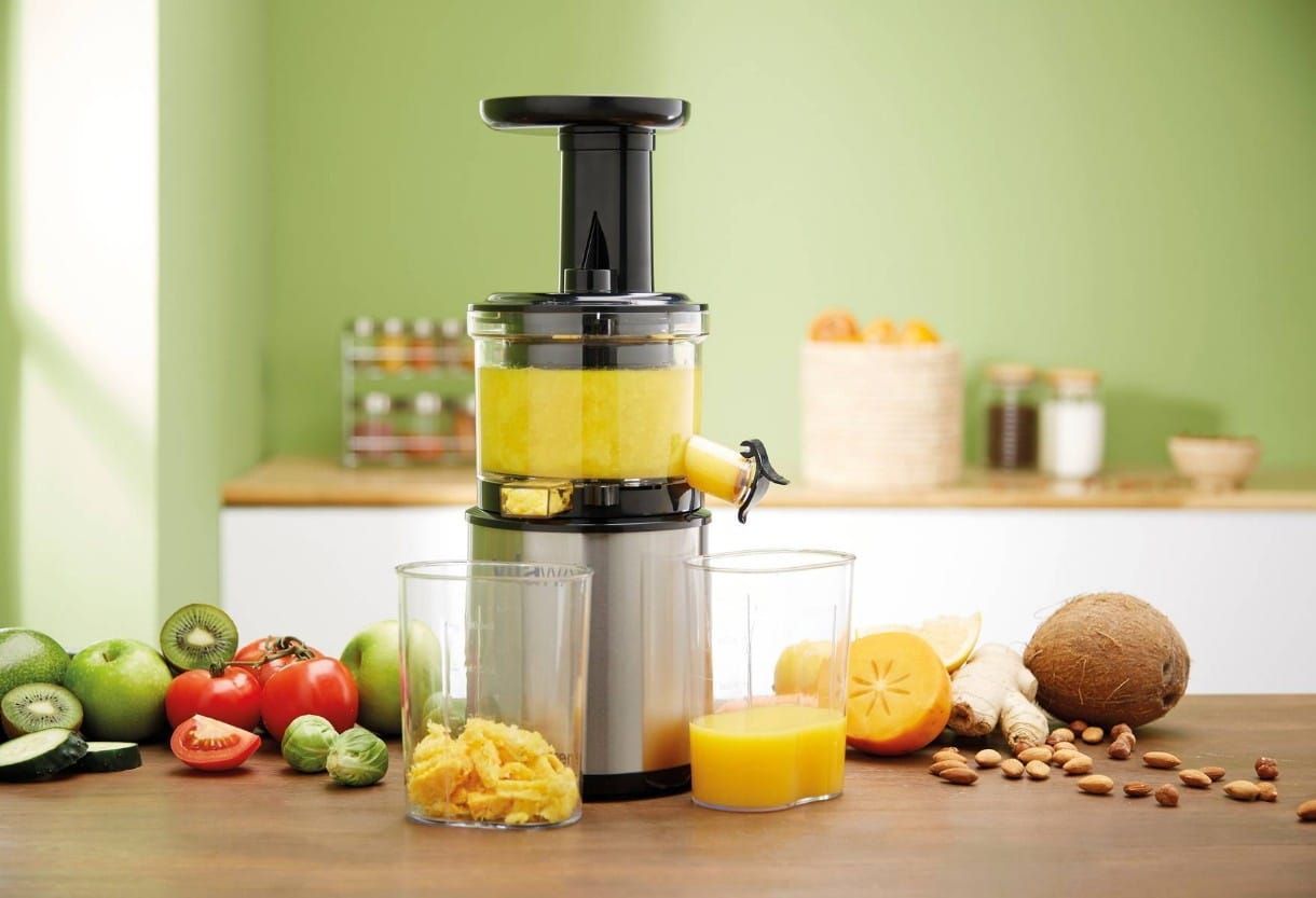 A juicer is sitting on a wooden table surrounded by fruits and vegetables.