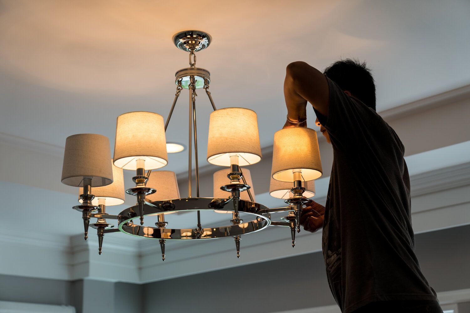 A man is hanging a chandelier from the ceiling in a room.