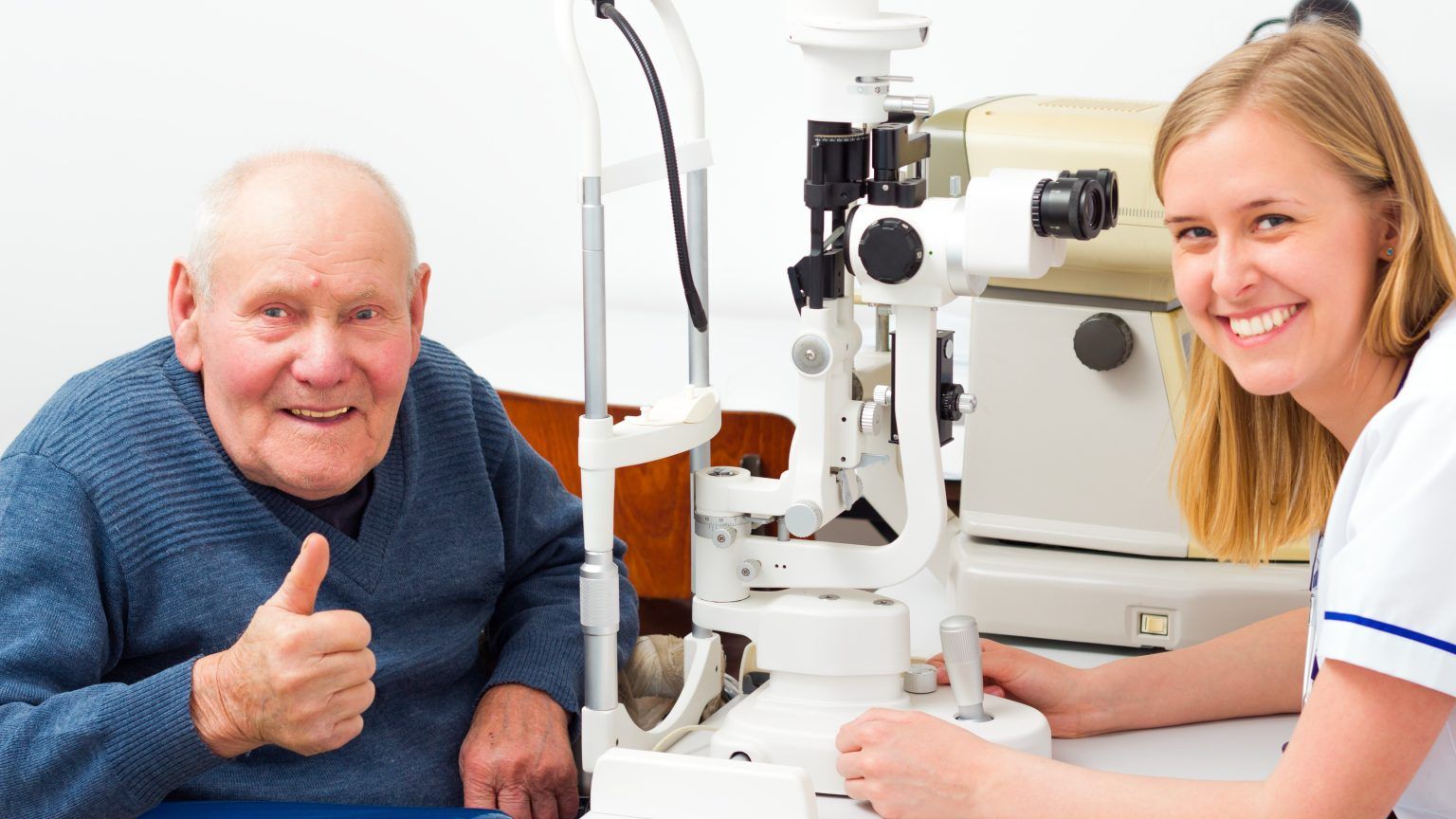 Elderly man with thumbs up at eye exam with smiling female doctor.