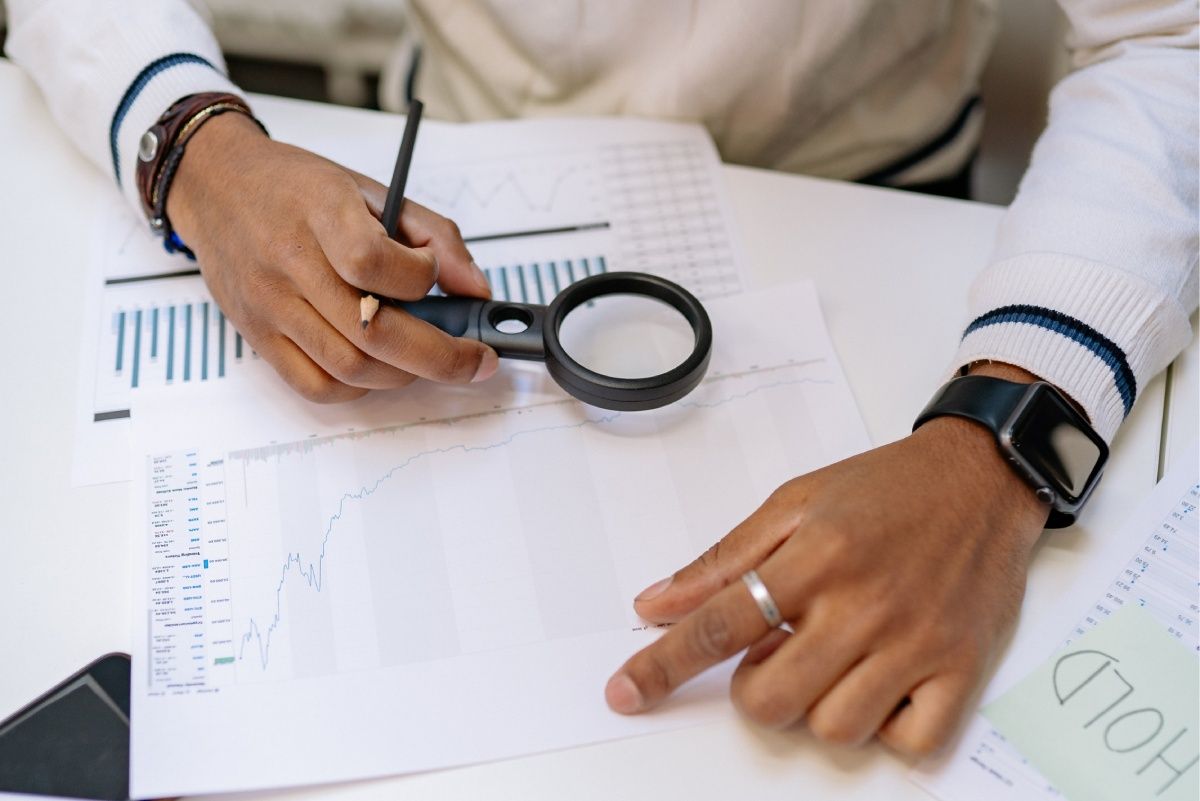 Person examining financial documents with a magnifying glass.