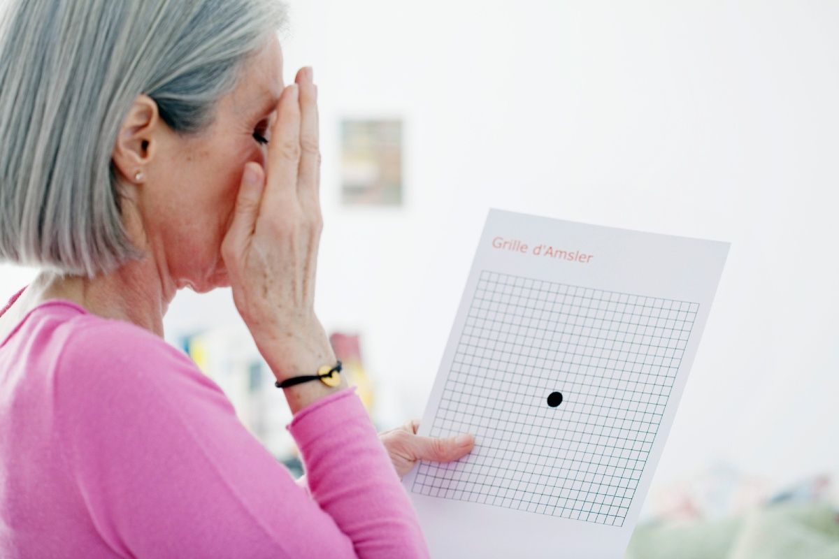 Woman with grey hair holding a vision test, covering one eye with her hand.