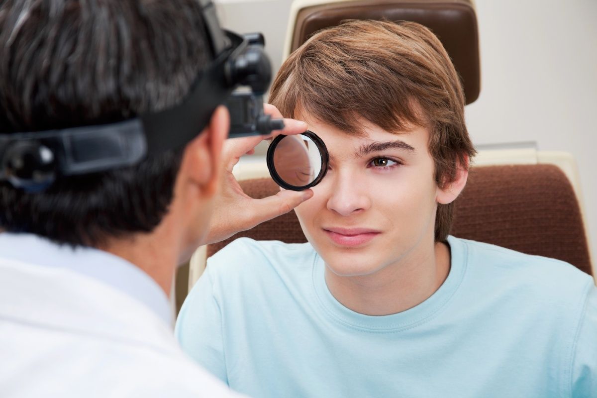A young man has his eyes examined by a doctor using a lens in a clinic setting.