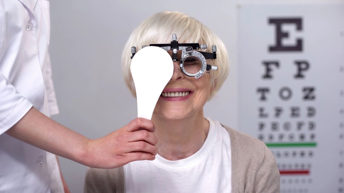 Optician closing one eye to smiling elderly woman in phoropter, perfect vision